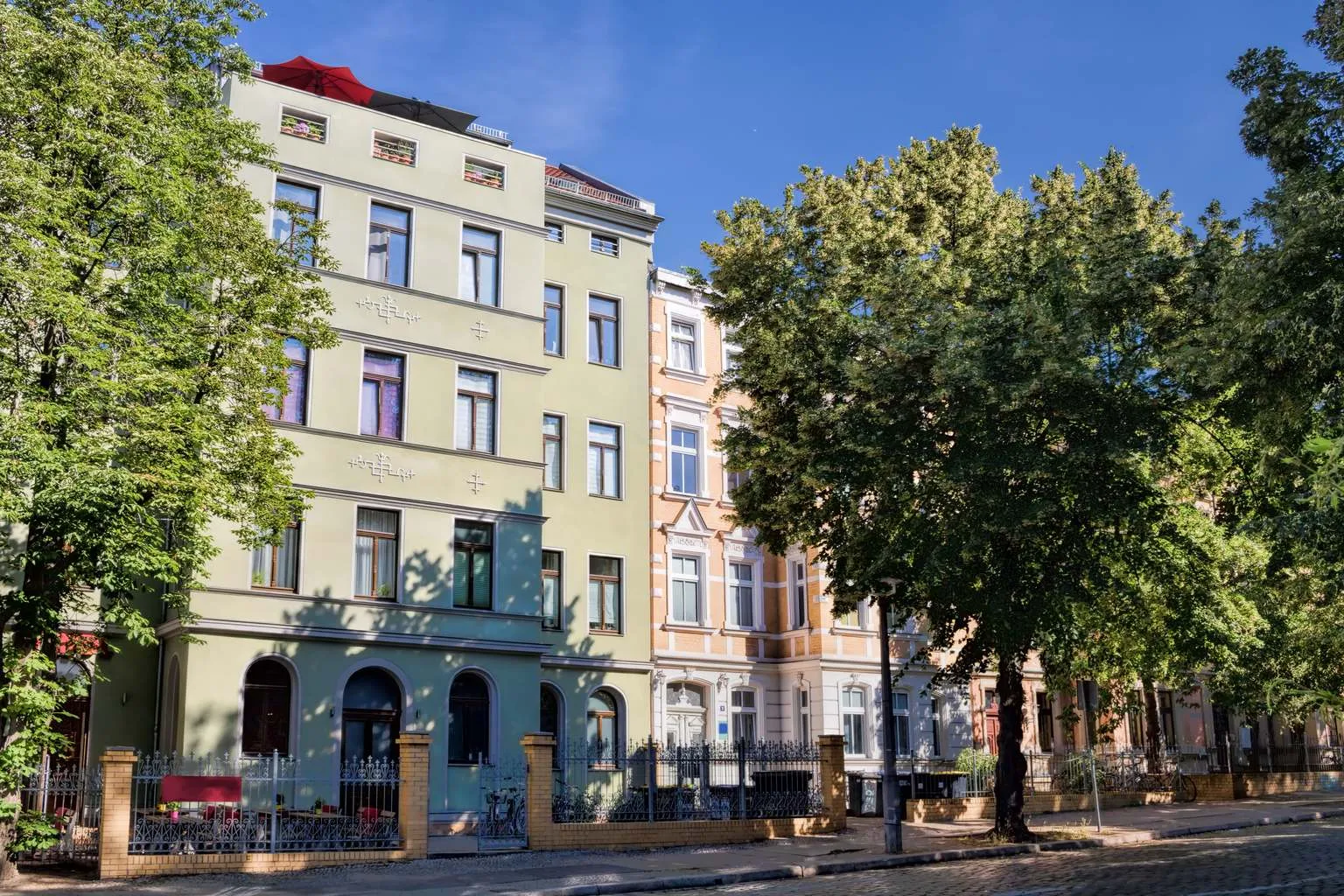 A row of restored classic German Altbau apartment buildings on a tree-lined residential street