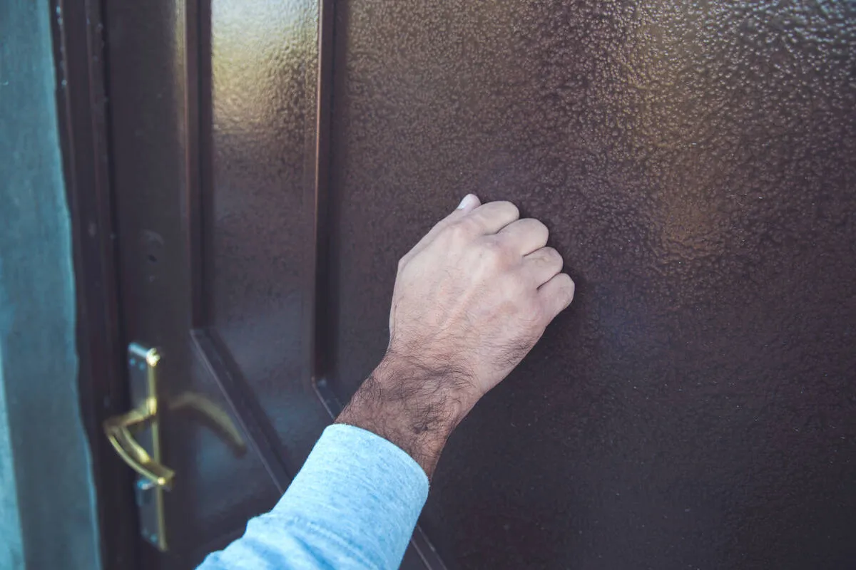 Close-up of a hand knocking on a tenant's apartment door, representing a maintenance visit
